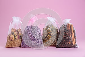 Scented sachets with dried flowers, coffee beans and spices on pink background