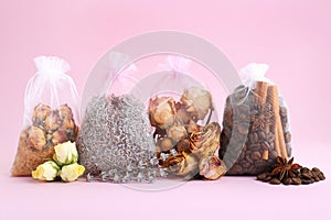 Scented sachets with dried flowers, coffee beans and spices on pink background