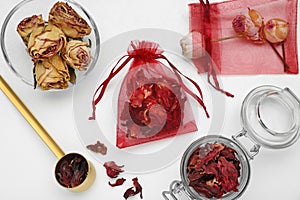 Scented sachets with dried rose and hibiscus flowers on white table, flat lay