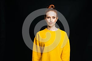 Sceptic disgruntled young woman wearing yellow sweater posing on isolated black background