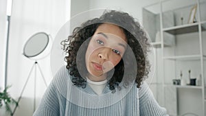 Sceptic young afro woman speaking to camera at home desk, Female on video call