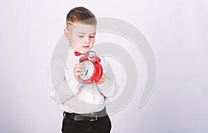 Schedule and timing. Morning routine. Schoolboy with alarm clock. Kid adorable boy white shirt red bow tie. Develop self