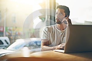 Scheduling a business meeting. A young man talking on the phone while sitting with his laptop in a coffee shop.