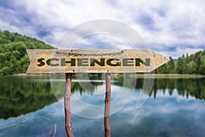 Schengen wooden arrow road sign against lake and forest background. Schengen  - European border control-free travel area