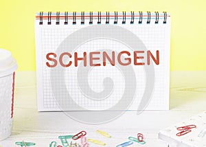 Schengen the word is written on a blank sheet in a notebook standing on a table on a yellow background