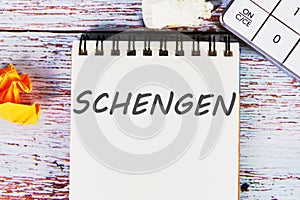 Schengen word written on a sheet of notebook lying on old vintage boards with a calculator and folded paper