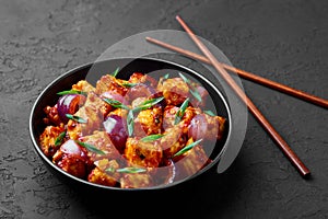 Schezwan Paneer in black bowl at dark slate background. Schezwan Paneer is indo-chinese cuisine dish