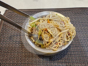 Schezwan or vegetable Hakka Noodles or chow mein is a popular Indo-Chinese recipes, served in a bowl or plate with fork. photo