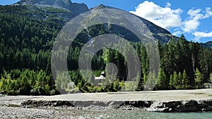 Schlierersee, Lungau Austria.Wooden chapel in pine trees on the shore of a mountain lake.Transparent green water of lake