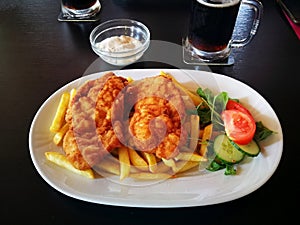 Schnitzels with fries, tartar souce and vegetables, on a white porcelain dish