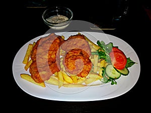 Schnitzels with fries, tartar souce and vegetables, on a white porcelain plate