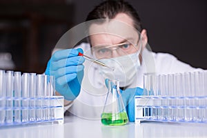 Scholar in mask and rubber gloves conducts researching in the lab. Scientist dripping by pipette green reactant into a