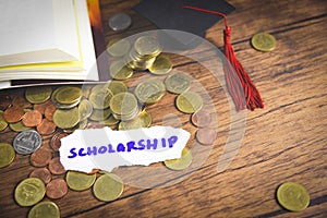 Scholarship for education concept with money coin on wooden with dark background and graduation cap on open book