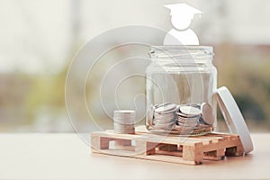 Scholarship money and saving for education concept. Coins in a jar with an icon of the man wearing a graduation cap.