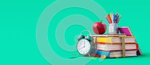School accessories with apple, books and alarm clock on green background. Back to school concept