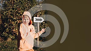 A school-age boy in the park shows the direction where to go and where the sign with the arrow shows