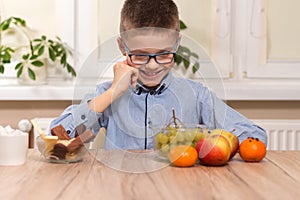 A school-age boy sits at a table and stares at the fruit lying on the table with a smile. The boy standing on the table ignores sw