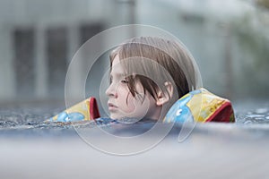 School-age child swims on the water surface of the pool