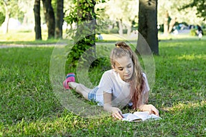 A school-age girl reading a book lying on the grass in the park