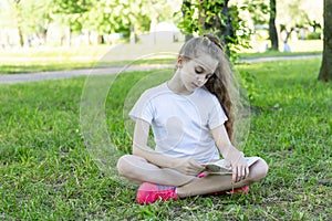 A school-age girl reading a book sitting on the grass in the park