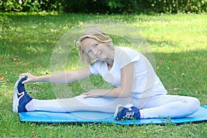 School-age kid girl in light clothes take sport exercise on a mat in the park. Outdoors workout.