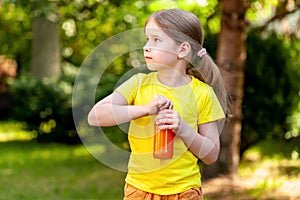 School age young child, happy little girl opening a glass bottle full of healthy orange carrot juice, simple outside outdoors