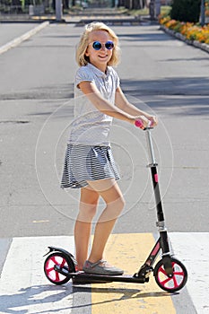 School-aged girl riding a scooter. Crosses the road on a pedestrian crossing.