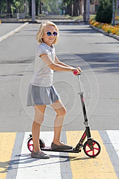 School-aged girl riding a scooter. Crosses the road on a pedestrian crossing.