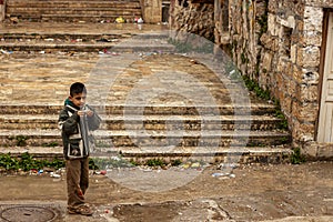A school aged Syrian boy is playing outside in a low income neighborhood on a rainy day.