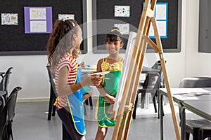 In school, in art class, biracial and a Caucasian girl, both young, are painting photo