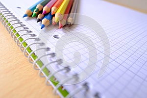 School background, colored pencils lie on a sheet of paper, an open notebook on a spiral, a college block in a cage, close-up, the
