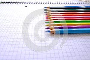 School background, colored pencils lie on a sheet of paper, an open notebook on a spiral, a college block in a cage, close-up, the