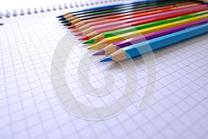 School background, colored pencils lie on a sheet of paper, an open notebook on a spiral, a college block in a cage, close-up, the