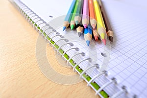 school background, colored pencils lie on a sheet of paper, an open notebook on a spiral, a college block in a cage, close-up, the