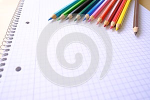 school background, colored pencils lie on a sheet of paper, an open notebook on a spiral, a college block in a cage, close-up, the