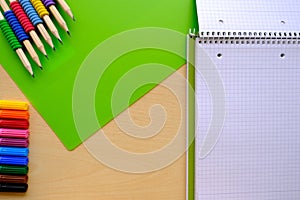 School background, colored pencils lie on a sheet of paper, open notebook on a spiral, college block in a cage, close-up, concept