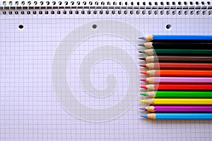 School background, colored pencils lie on a sheet of paper, open notebook on a spiral, college block in a cage, close-up, concept