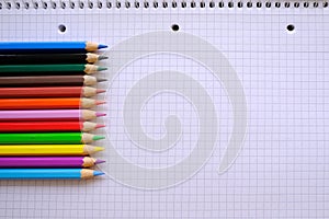school background, colored pencils lie on a sheet of paper, open notebook on a spiral, college block in a cage, close-up, concept