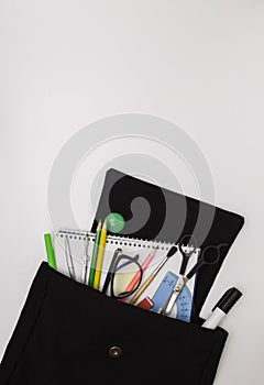 School background. Office supplies in an open black backpack. White background, free space for text