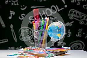School background with stationery accessories. Books, globe, pencils and various office supplies lying on the desk on a green