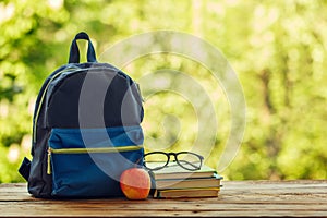 School backpack with books on wooden table and nature background