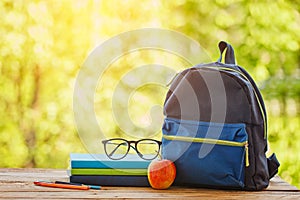 School backpack with books on wooden table and nature background