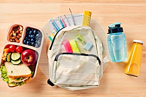 School backpack with supplies, kids lunch box with sandwich, fruits, vegetables, bottles of water and juice on wooden table