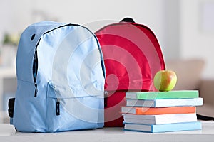 School backpacks with notebooks and apple on table