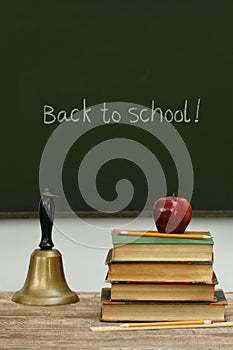 School bell and books on desk with chalkboard