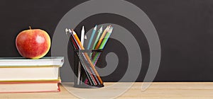 School books, apple and pencils over chalkboard background