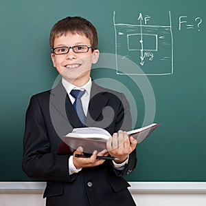School boy with book, archimedes principle drawing on chalkboard background, dressed in classic black suit, education concept