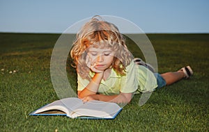School boy with a book having a rest outdoor. Child boy is reading a book on the spring park. Relaxing on the grass in
