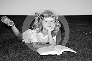 School boy with a book having a rest outdoor. Clever child boy reading book laying on grass on grass and sky background