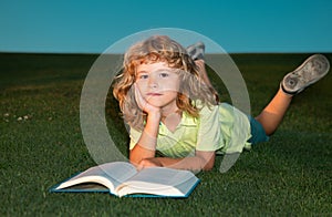 School boy with a book having a rest outdoor. Clever child boy reading book laying on grass on grass and sky background